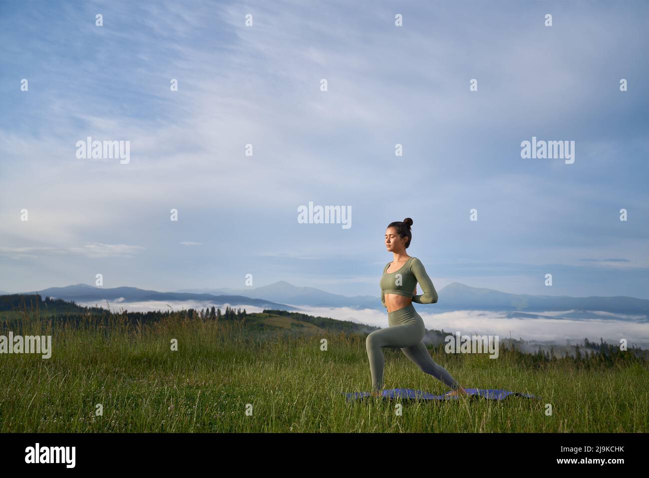 Sportliche junge Frau im aktiven Ohr, die morgens Zeit für Yoga-Übungen in den Sommerbergen verbringt. Konzept von Menschen und aktiven Lebensstilen. Stockfoto