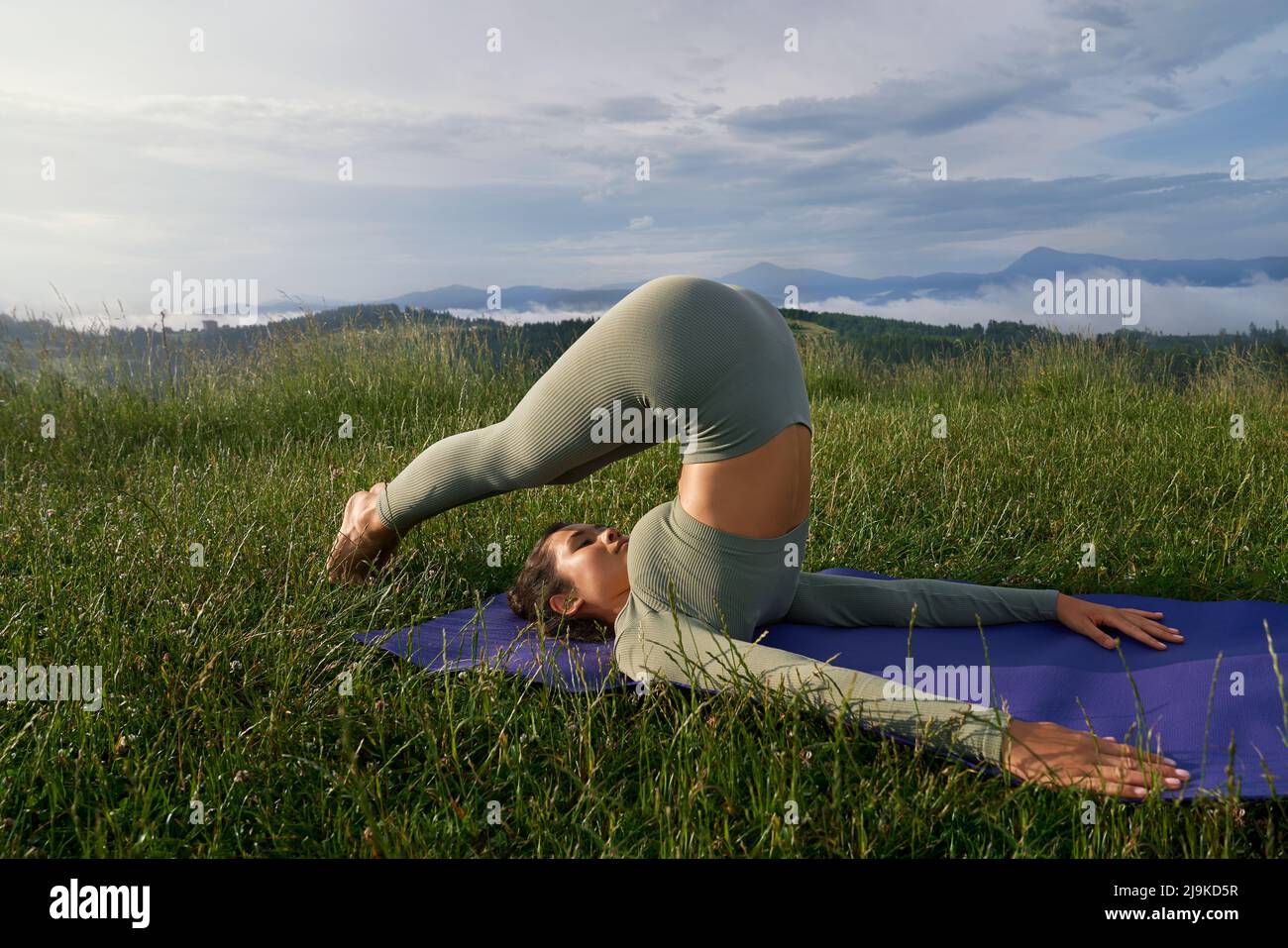 Charmante sportliche Frau in der aktiven unterwegs Stretching für Körper auf Yoga-Matte inmitten der grünen Natur. Outdoor-Aktivitäten und gesunde Lebensstile Konzept. Stockfoto
