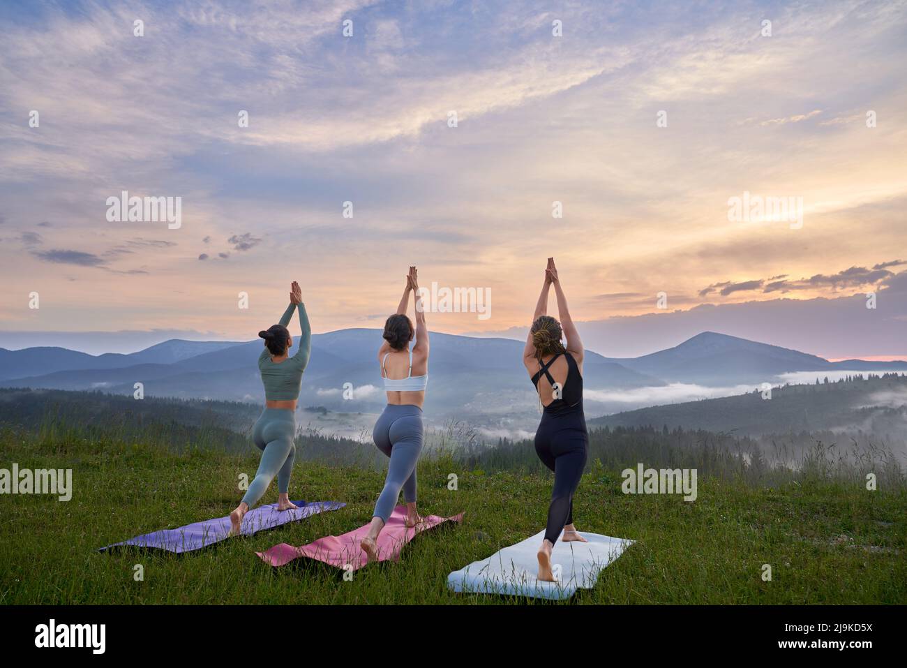 Eine Gruppe von drei sportlichen Frauen im aktiven Ohr, die im Sommer im Freien gemeinsam meditieren. Abends Zeit für Yoga-Übungen. Stockfoto