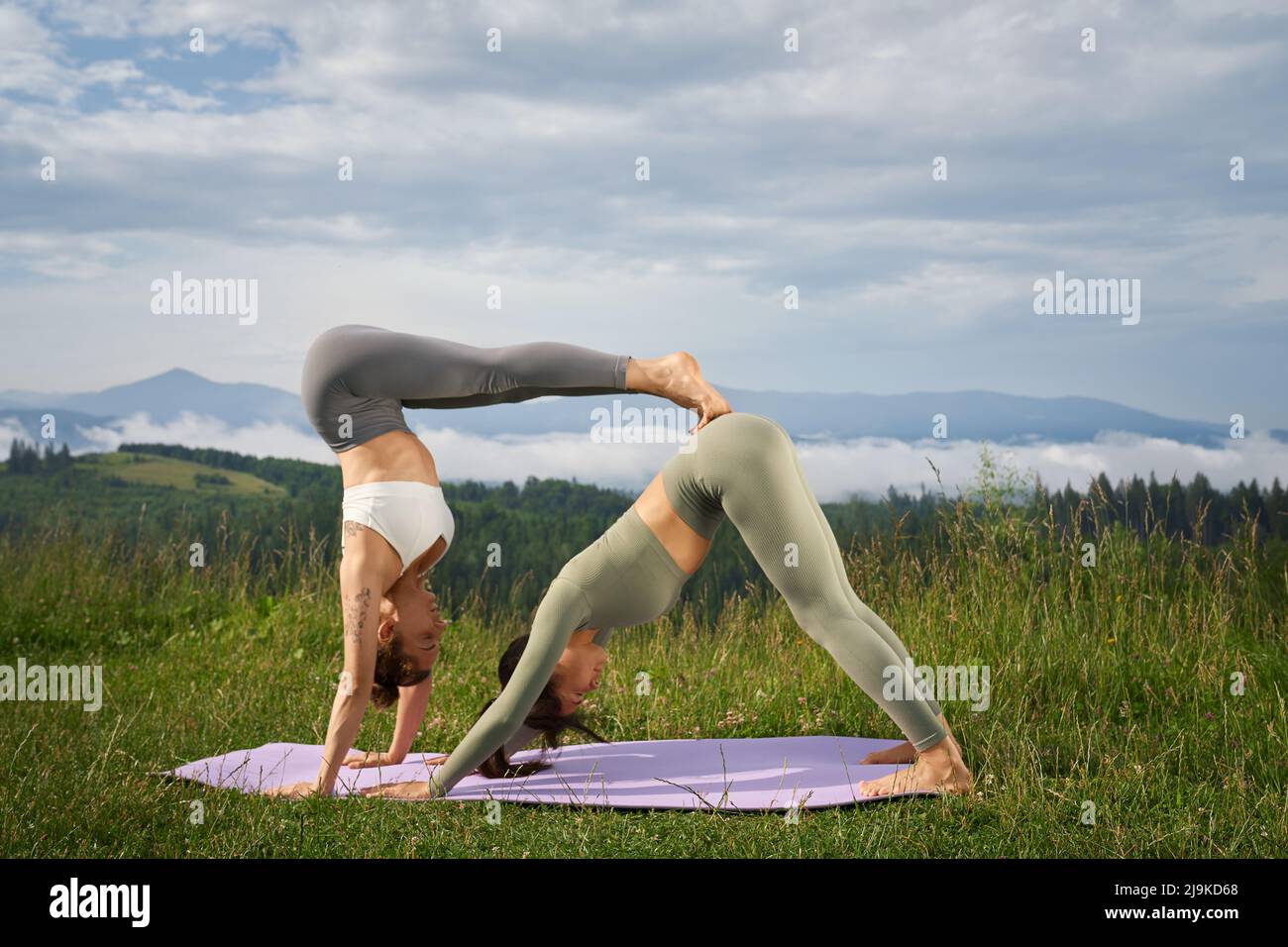 Fitness kaukasische Frauen in Sportkleidung trainieren gemeinsam auf einer Yogamatte inmitten wunderschöner Sommerberge. Zwei Freunde führen einen aktiven und gesunden Lebensstil. Stockfoto
