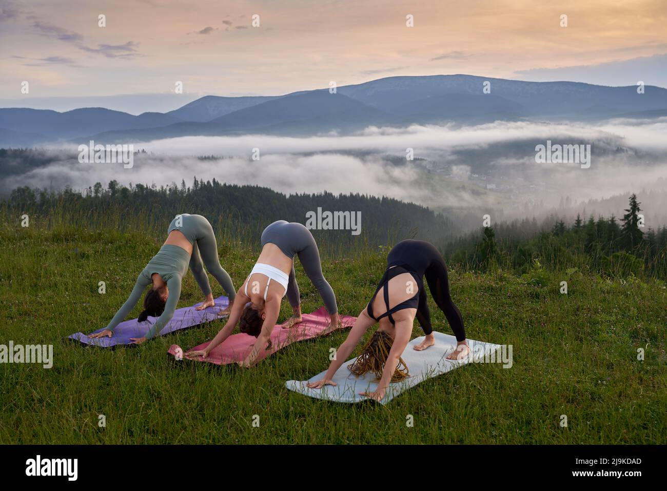Sportliche und gesunde Frauen trainieren gemeinsam auf einer Yogamatte im Sommer in den Bergen aktiv. Konzept von Menschen, Training und Wohlbefinden. Stockfoto