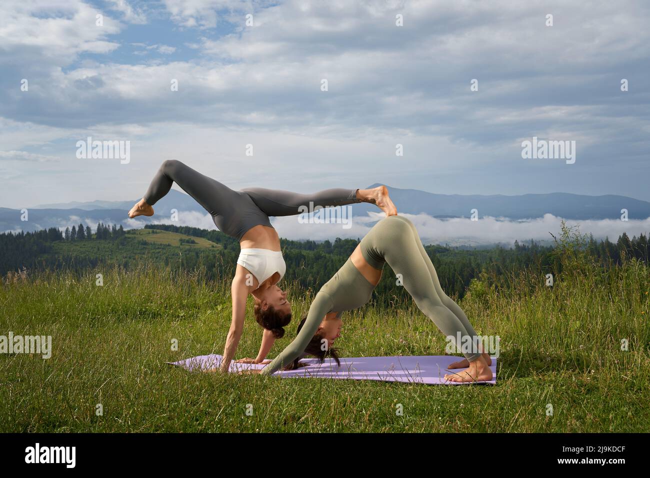 Gesunde und fit junge Frauen in Sportkleidung, die aktiv an der frischen Luft trainieren. Zwei Freundinnen üben Yoga mit Blick auf die Berge im Hintergrund. Stockfoto