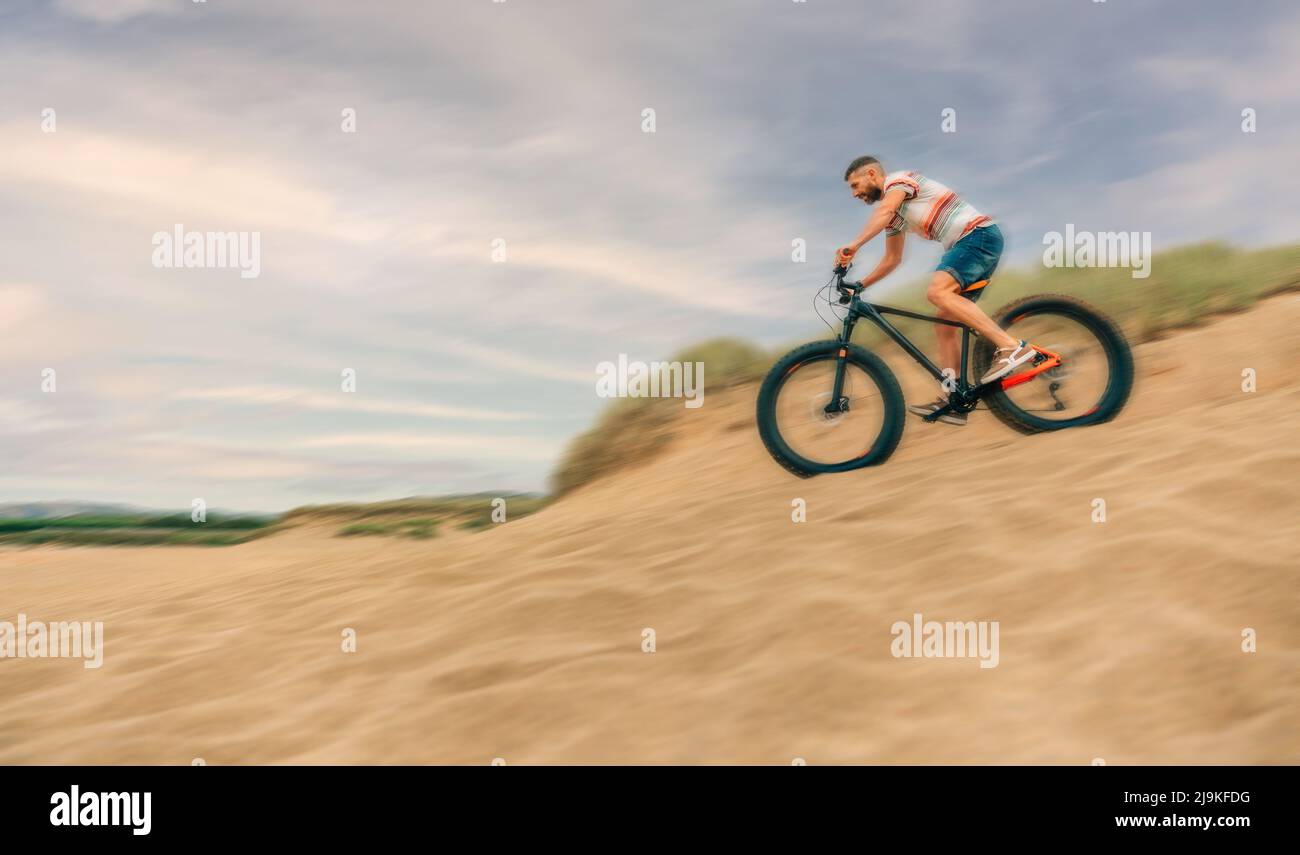 Mann, der schnell fette Fahrräder durch Stranddünen fährt Stockfoto