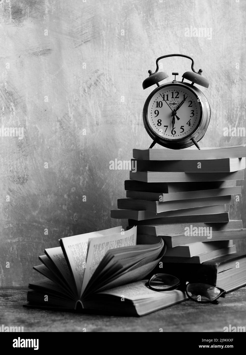 Stapel alter Bücher, Vintage-Uhr auf einem Schreibtisch. Hellgrauer strukturierter Hintergrund mit Kopierbereich. Bildungskonzept. Stockfoto