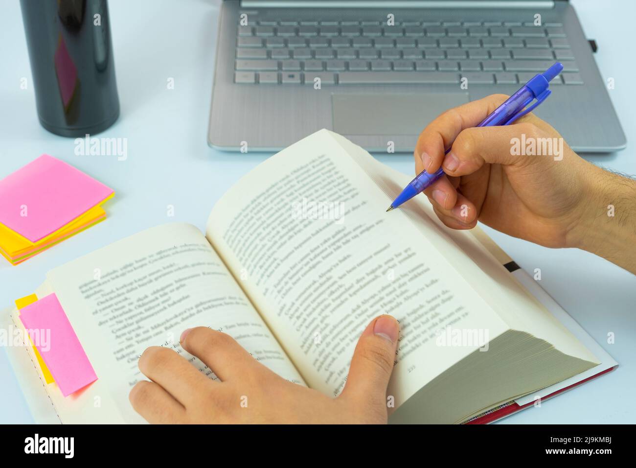 Laptop und offenes Buch mit violettem Bleistift isoliert auf weißem Hintergrund, Studium und Arbeitskonzept, konzentrieren sich auf das Lesen, Notizen machen, sitzende Ansicht Stockfoto