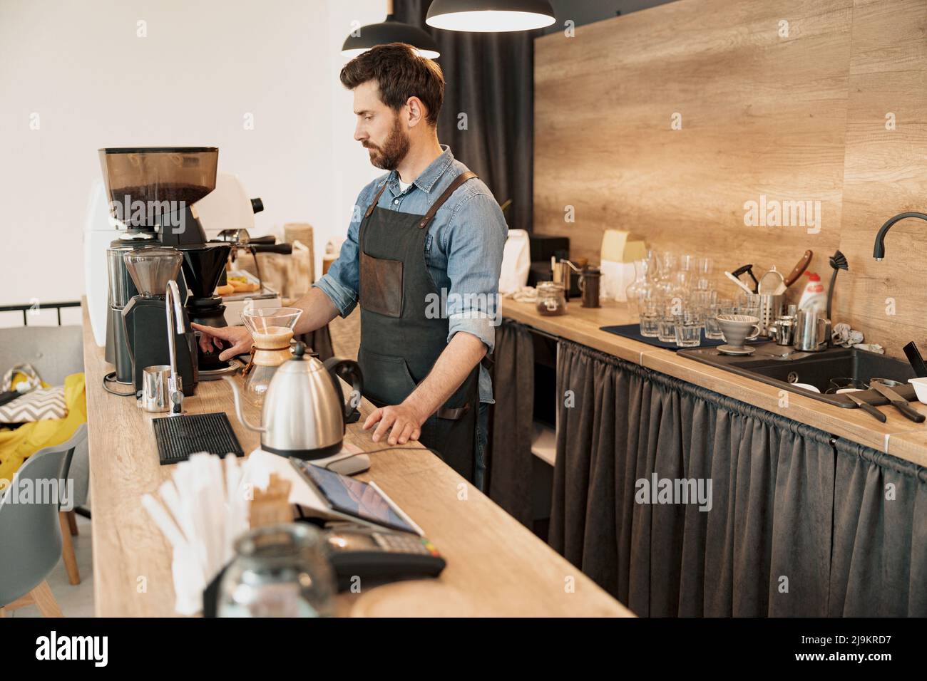 Der gutaussehende Barista mahlt Kaffeebohnen in der Kaffeemaschine Stockfoto