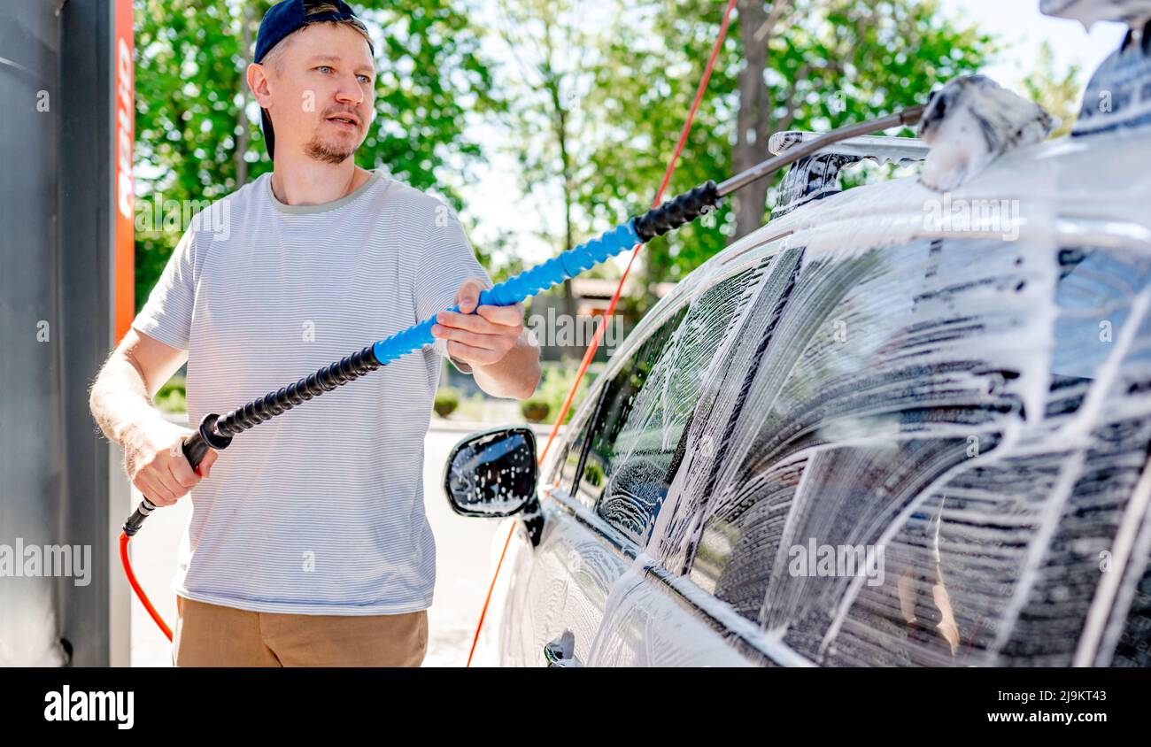 Ein Mann, der bei einer Selbstbedienungswaschung ein Auto wäscht Stockfoto