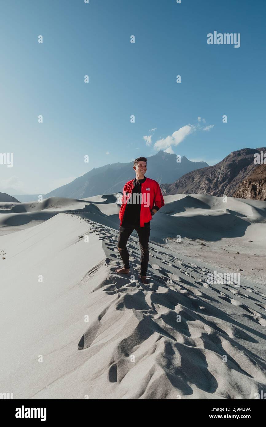Junger männlicher Tourist auf einer Sanddüne mit einer leuchtend roten amerikanischen Jacke in der kalten Wüste von skardu pakistan Stockfoto