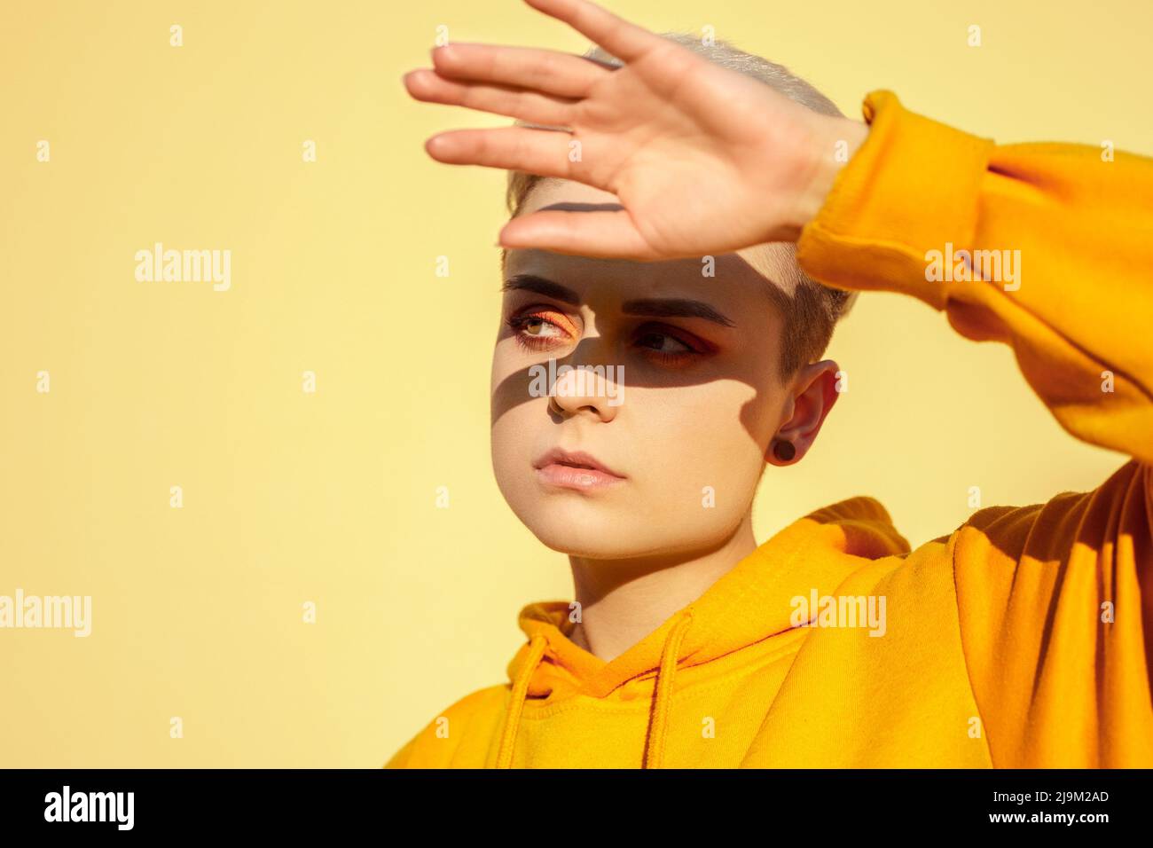 Junge Teenager-Hipster-Frau bedeckt die Augen vor Sonnenschein über der gelben Wand Stockfoto