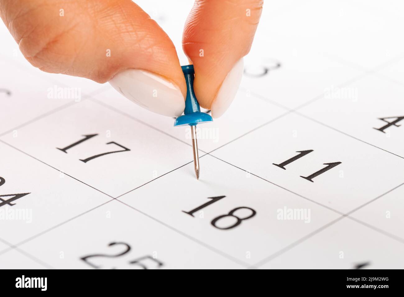 Schöne weibliche Hand mit Maniküre schiebt eine blaue Nadel auf einen Kalender Stockfoto