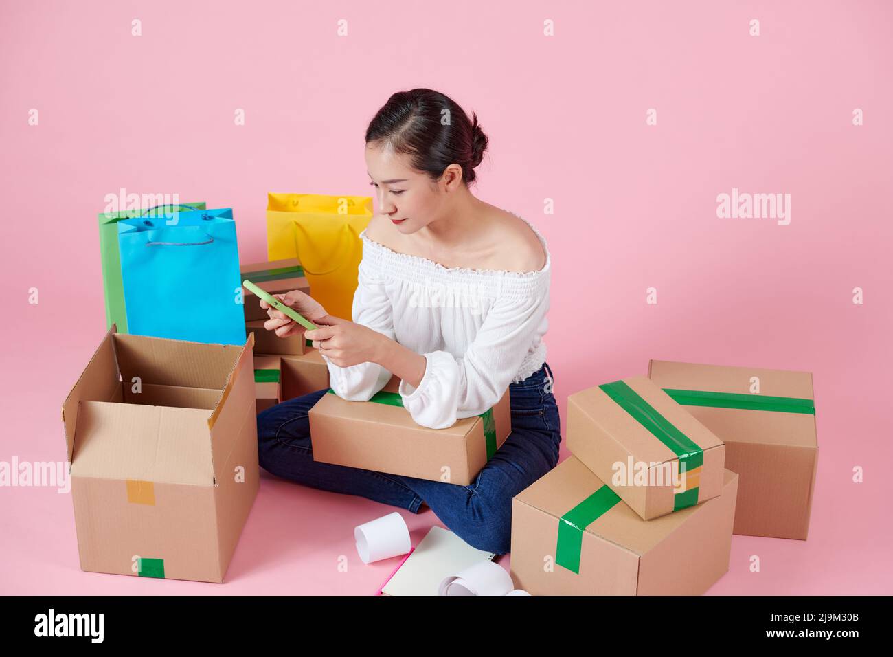 Junge asiatische Geschäftsfrau nutzt Ihr Smartphone, bekommt eine Bestellung von Kunden, macht sich Notizen und arrangiert die Lieferung per Post. Stockfoto