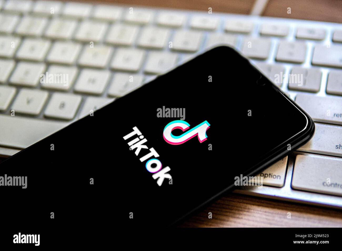 In dieser Abbildung wird ein TikTok-Logo auf einem Smartphone angezeigt, das auf einer Computertastatur platziert ist. Stockfoto
