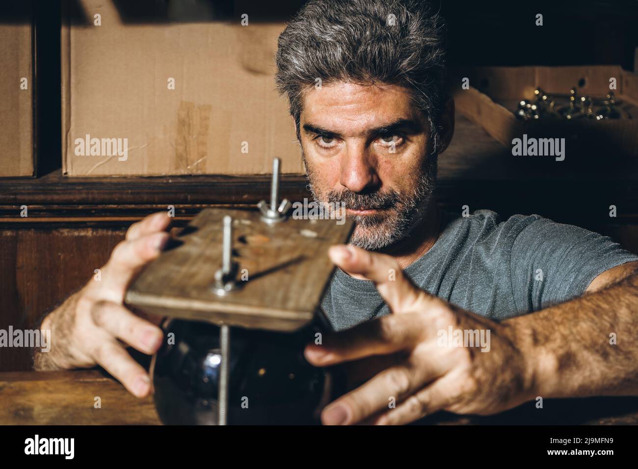 Serious reifen Handwerker in grau T-Shirt Anpassung schwarzen Keramikbecher in Holzpresse auf der Werkbank während der Arbeit in grungy Werkstatt Stockfoto