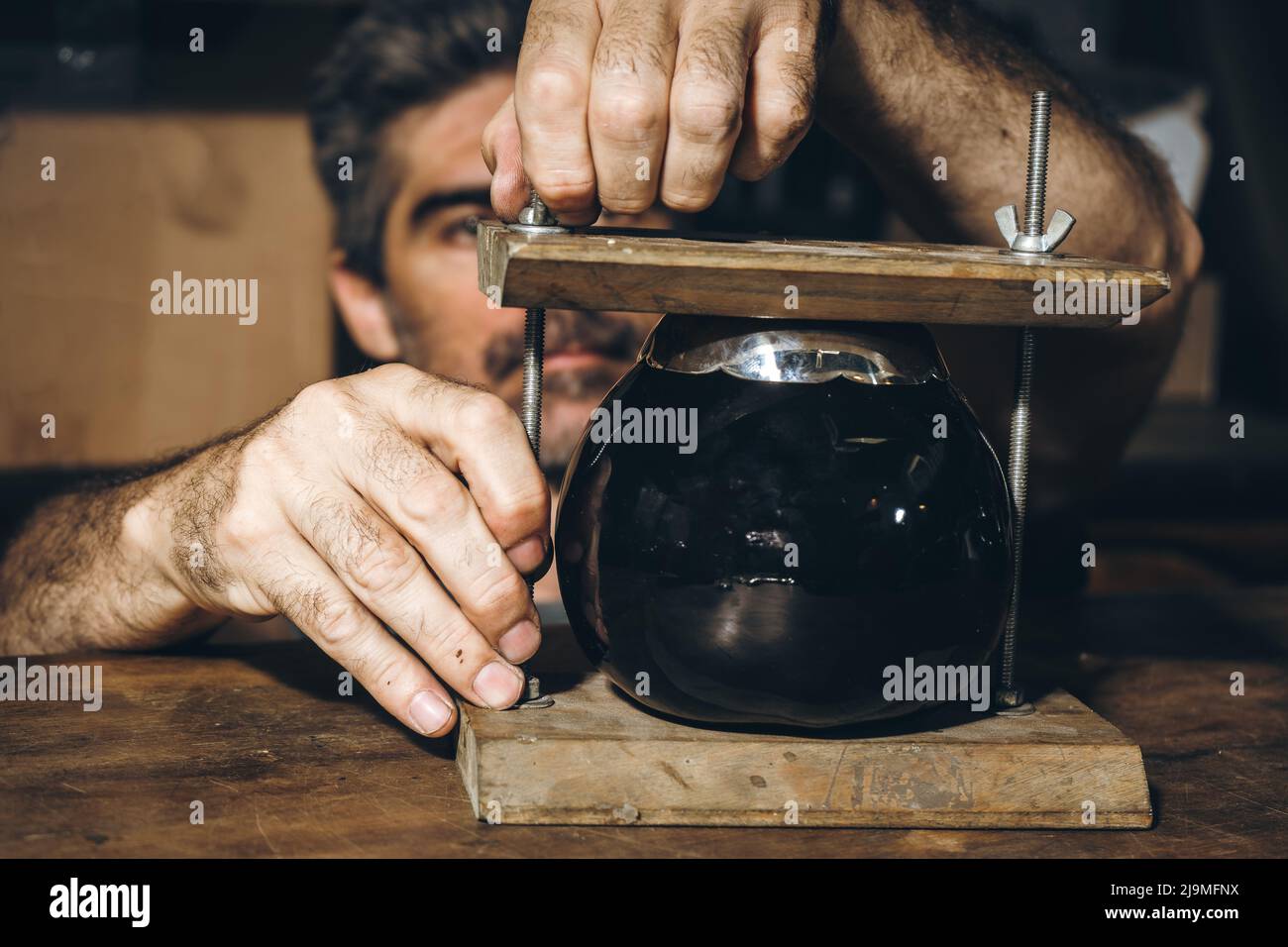 Serious reifen Handwerker in grau T-Shirt Anpassung schwarzen Keramikbecher in Holzpresse auf der Werkbank während der Arbeit in grungy Werkstatt Stockfoto