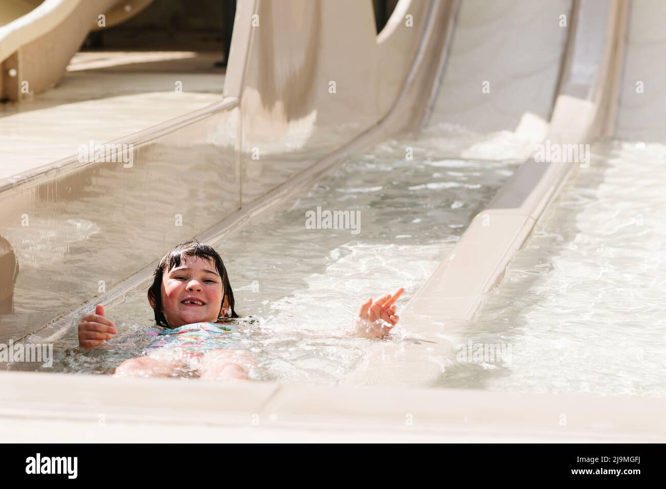 Von oben kleines Mädchen mit nassem dunklen Haar, das auf einer Wasserrutsche reitet, während es einen sonnigen Sommertag im Wasserpark verbringt Stockfoto
