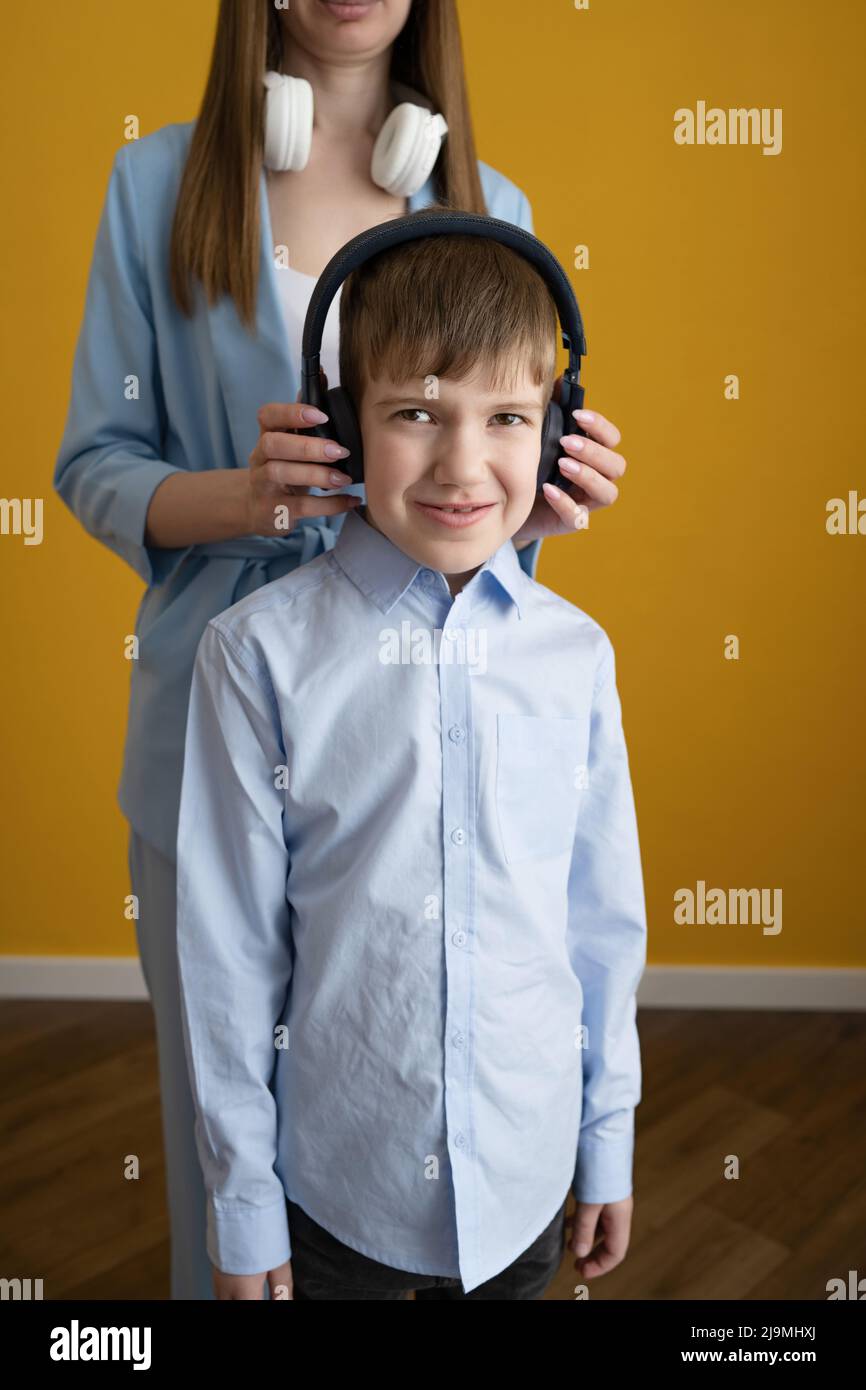 Crop Mother passt kabellose Kopfhörer auf Glad Son an, während sie zu Hause gemeinsam Musik an der gelben Wand hört Stockfoto