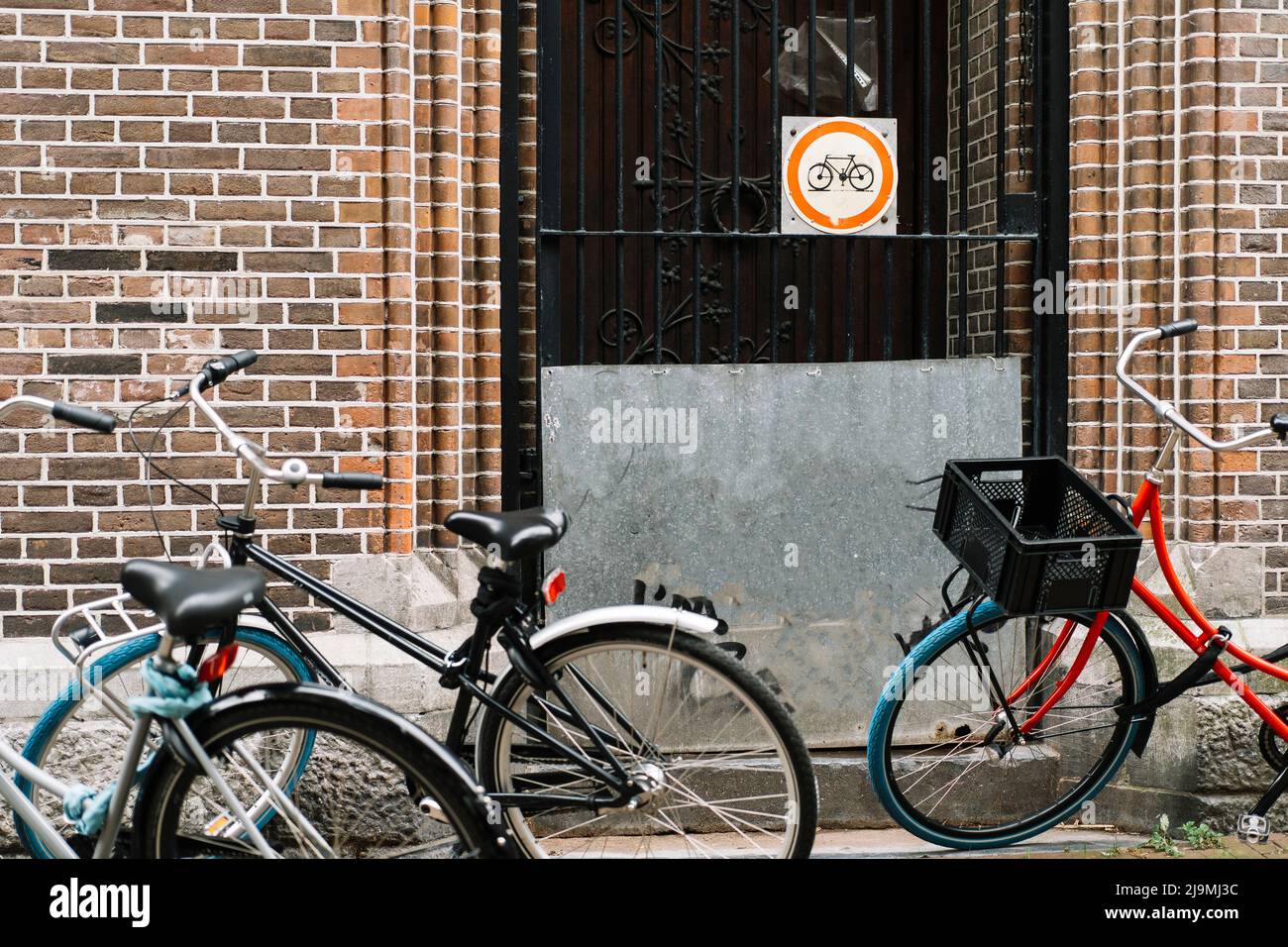Verschiedene moderne Fahrräder geparkt in der Nähe Zaun des Backsteingebäudes auf der Straße von Amsterdam am Tag Stockfoto