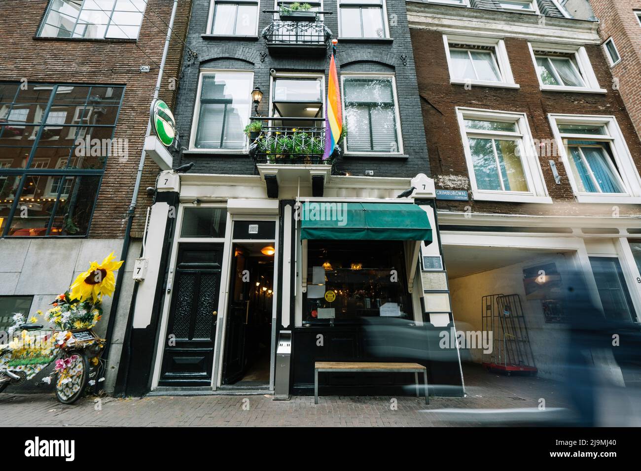 Von unten die LGBT-Regenbogenfahne, die an einem gemauerten Wohnhaus mit Fenstern und geschmiedeten Balkonen in Amsterdam hängt Stockfoto