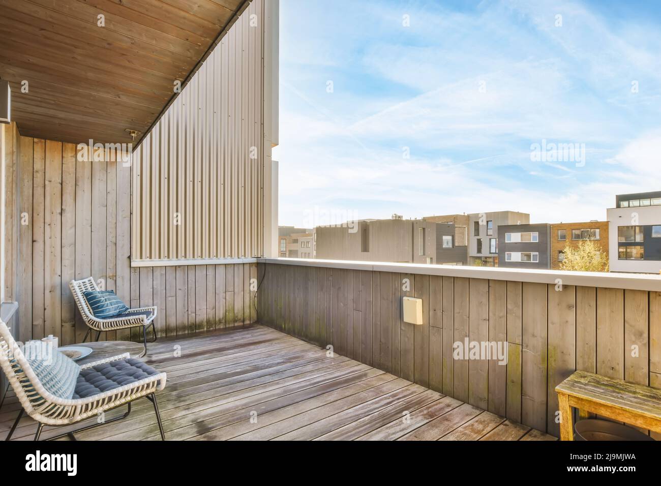 Bequeme Sessel und kleiner Tisch auf Holzterrasse in der Nähe der Wand des Wohnhauses in Vorort mit klarem blauen Himmel platziert Stockfoto