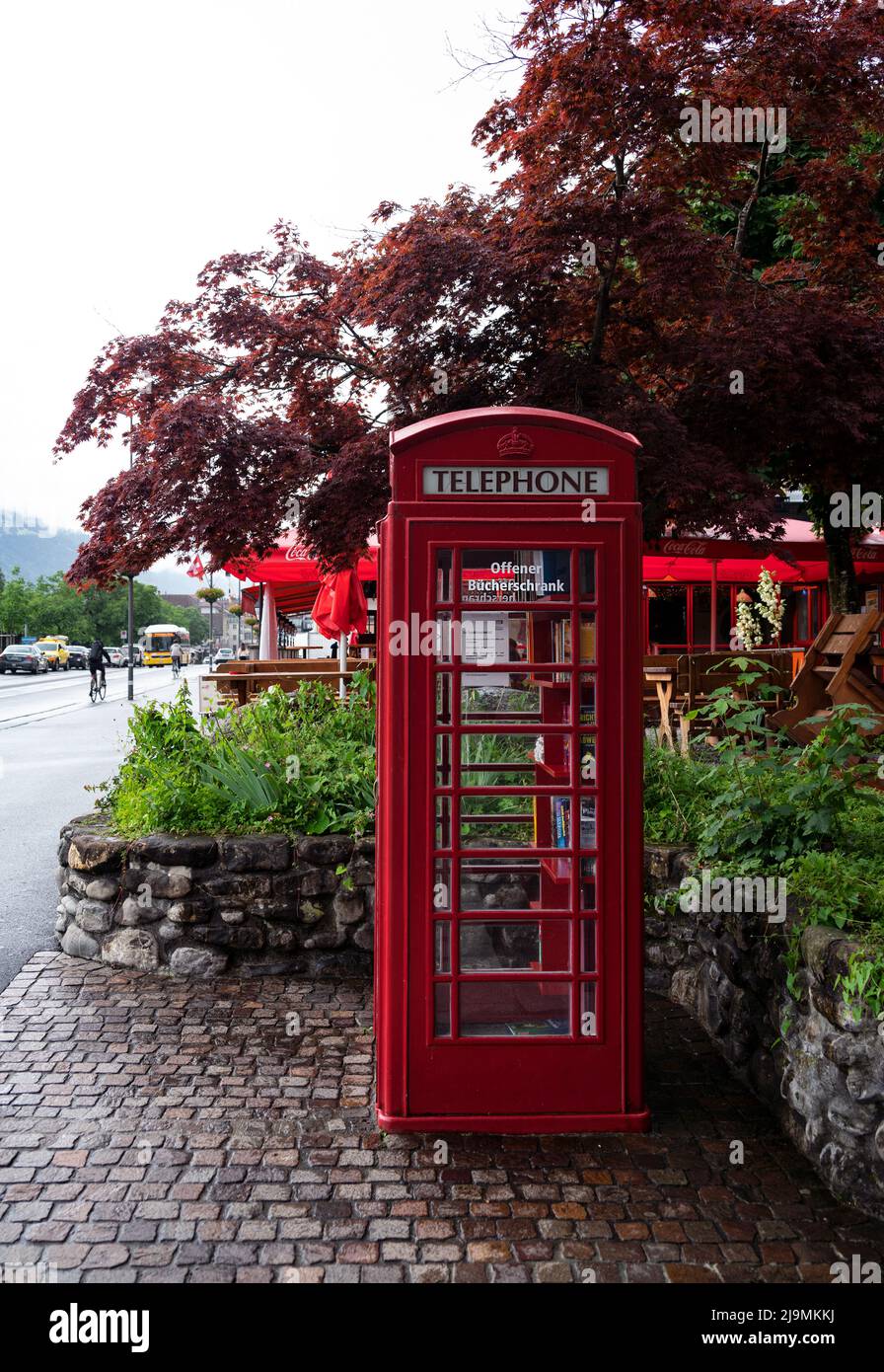 Blick auf ein öffentliches Swisscom-Telefon im klassischen britischen Stil in roter Telefonzelle mit einer offenen Bücherei in der Hauptstraße von Interlaken Stockfoto