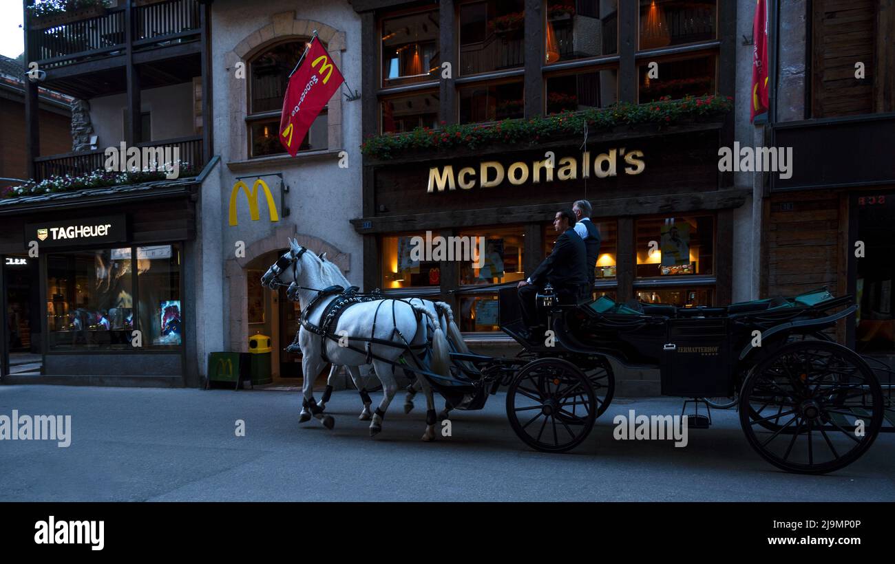 Mit dem Pferdebus fahren Touristen auf der Haupteinkaufsstraße von Zermatt, einem umweltfreundlichen autofreien Dorf, das von Restaurants und Geschäften umgeben ist Stockfoto