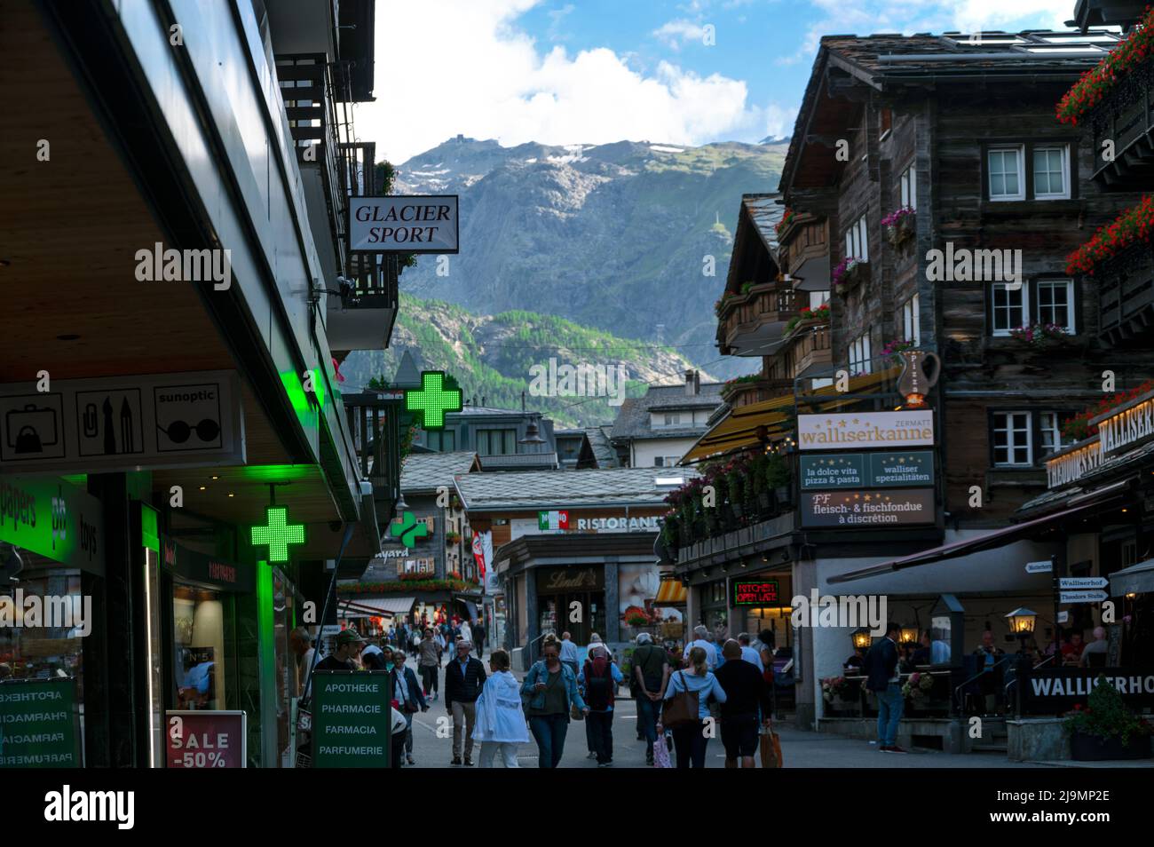 Die malerische Haupteinkaufsstraße von Zermatt mit Restaurants, lokalen Chalet-Häusern, Hotels und Geschäften voller Touristen im Sommer Stockfoto