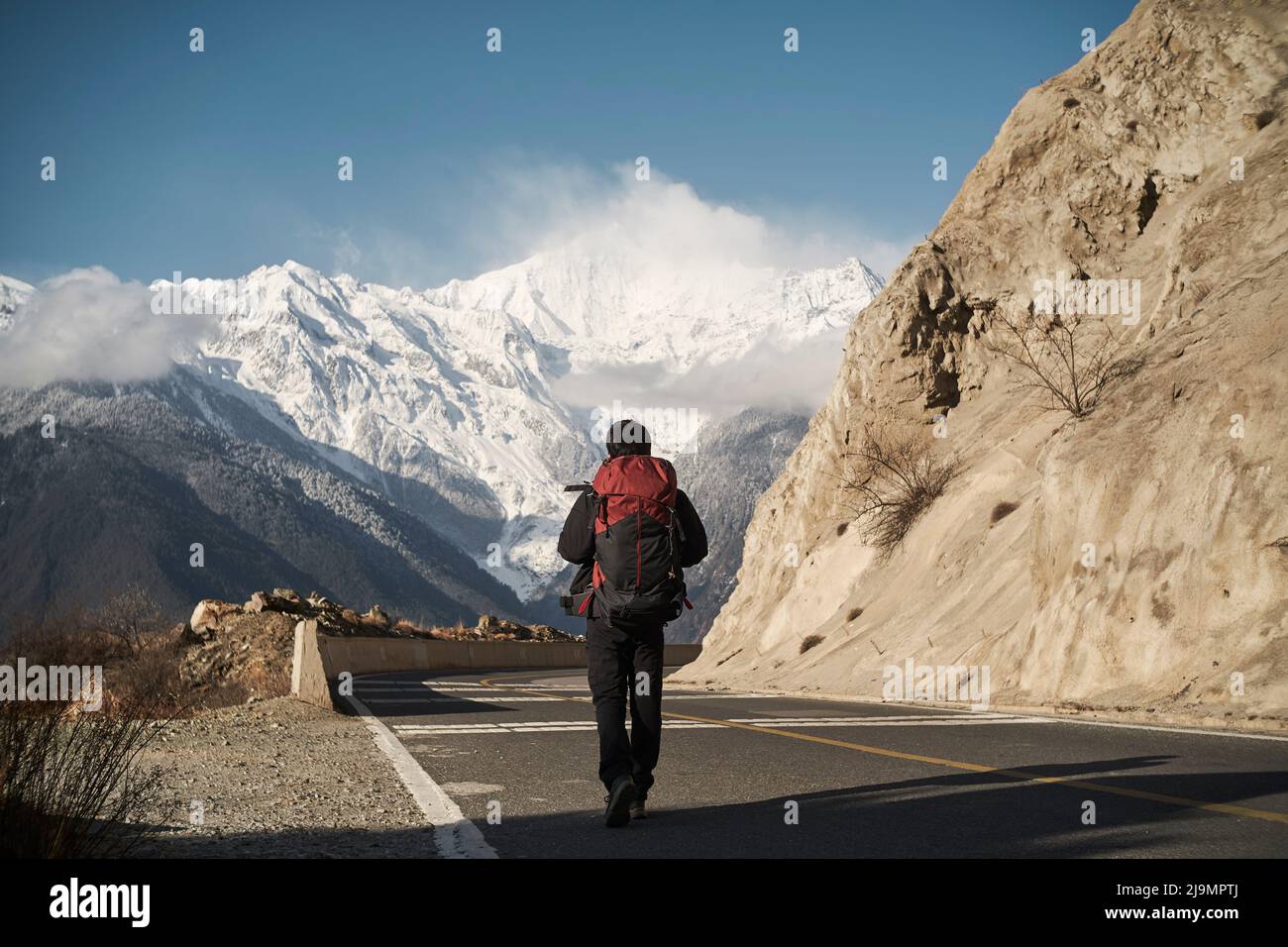 Rückansicht eines asiatischen Wanderers mit Rucksack, der auf der Autobahn mit schneebedeckter meili-Berg im Hintergrund läuft Stockfoto
