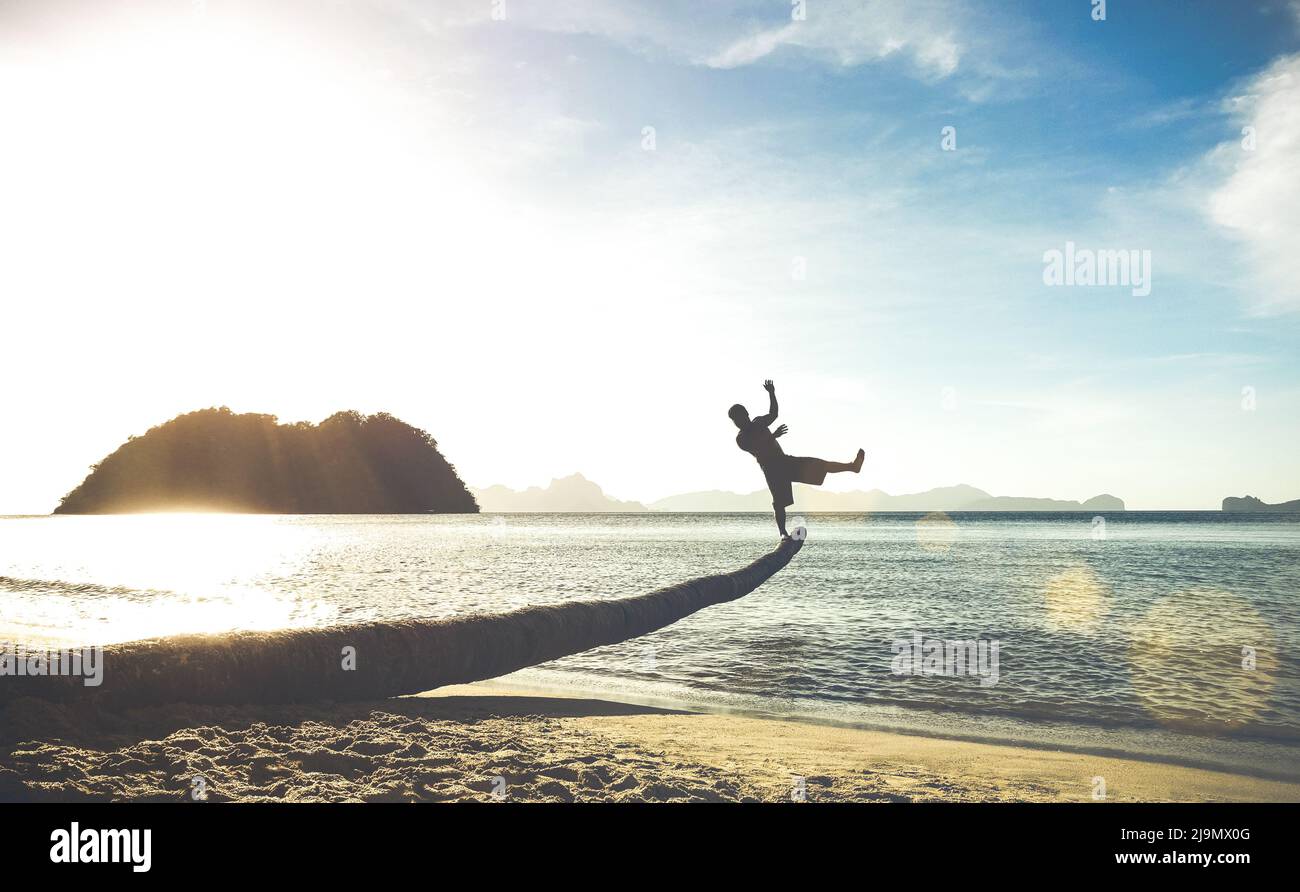 Silhouette eines Reisenden Kerl auf lustigen Sprung von der Palme - Reise-Fernweh-Konzept mit Mann, der Spaß am Las Cabanas Strand in El Nido Palawan - Soft Tilt Stockfoto