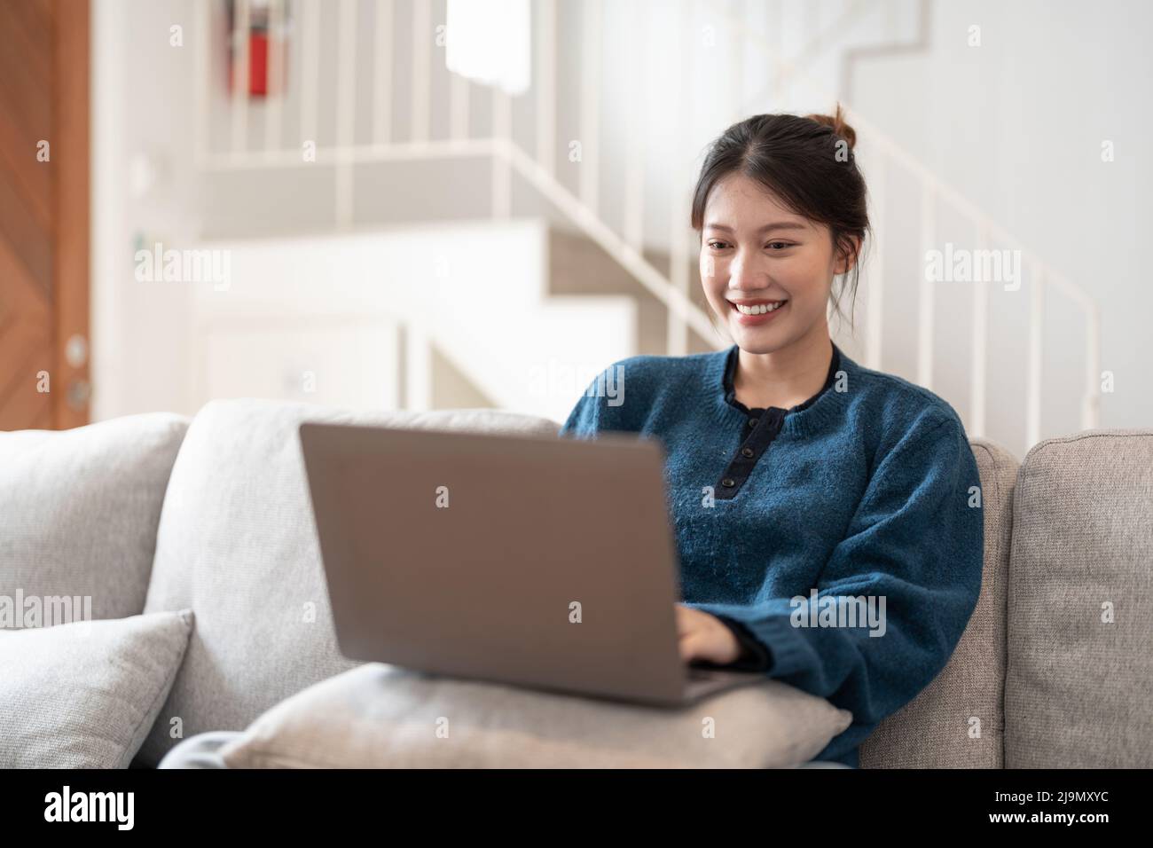 Happy Casual schöne junge asiatische Frau, die auf einem Laptop auf der Couch im Haus sitzt. Stockfoto