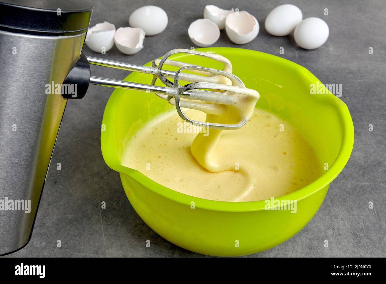 Eier mit Zucker und Mehl in einer grünen Schüssel und einem Mixer verprügelt Stockfoto