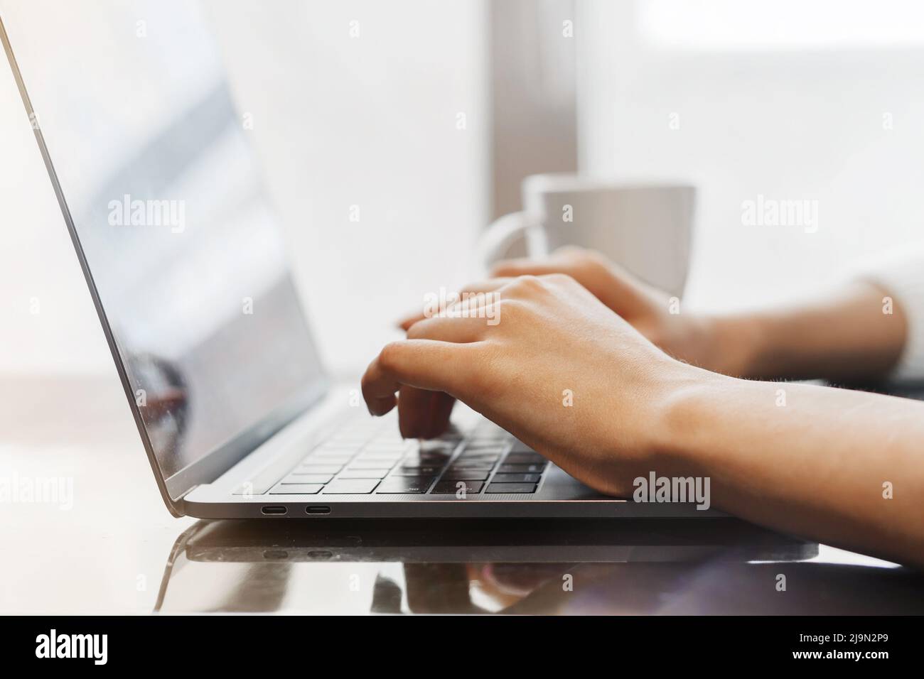 Nahaufnahme der Hände einer jungen Frau, die in einem Café auf einem Laptop tippt. Freiberufler arbeitet in einem Café. Laptop, Hände und Kaffeebecher Stockfoto