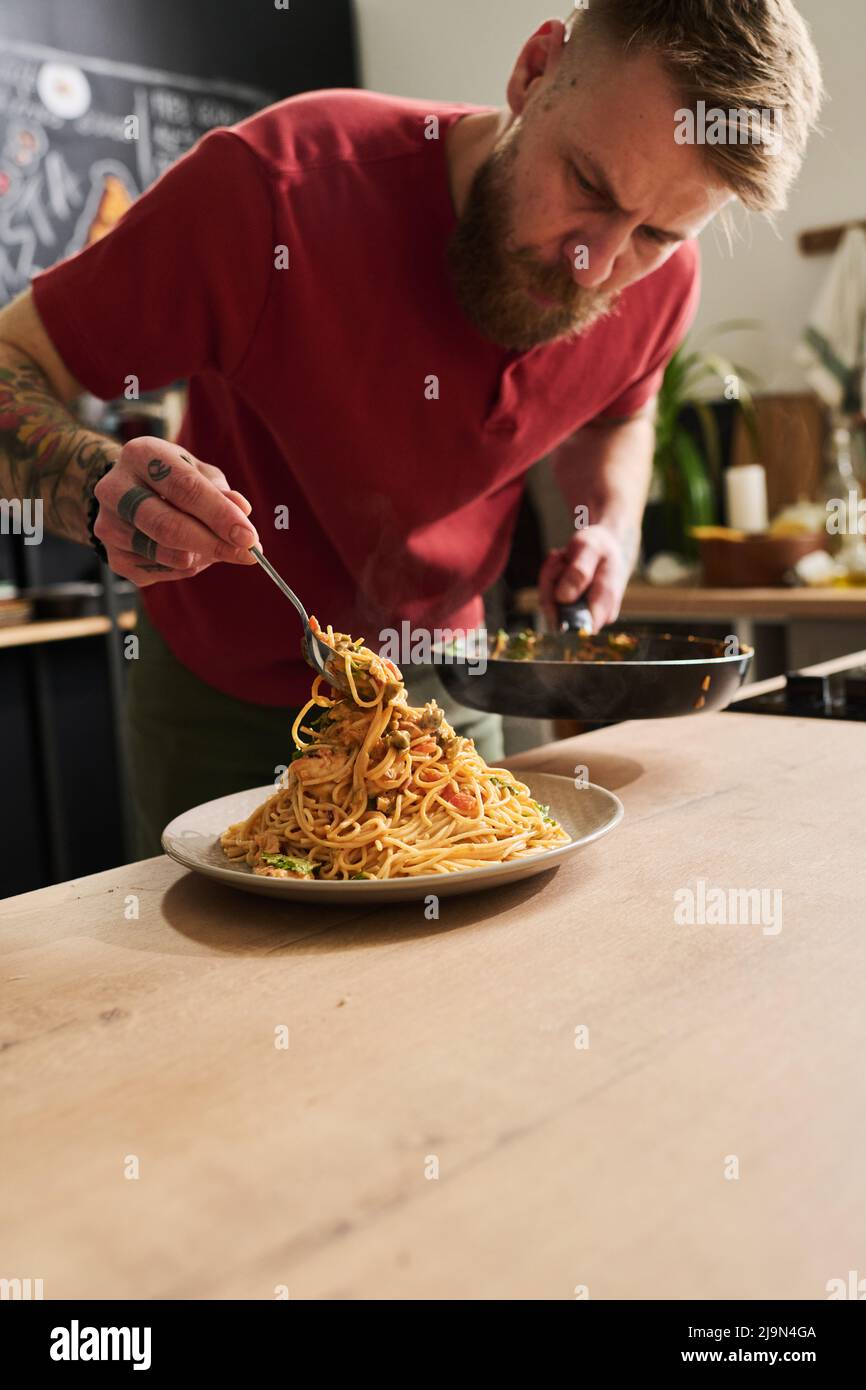 Moderne kaukasische Food-Blogger stehen in der Loft-Küche serviert heiße Pasta aus der Pfanne auf den Teller Stockfoto