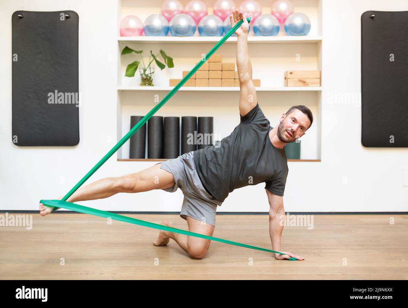 Der ganze Körper des barfuß-männlichen Athleten macht beim Training auf dem Boden im modernen Fitnessstudio eine seitliche Kick-Übung mit Gummiband. Man Fitness Konzept. Stockfoto