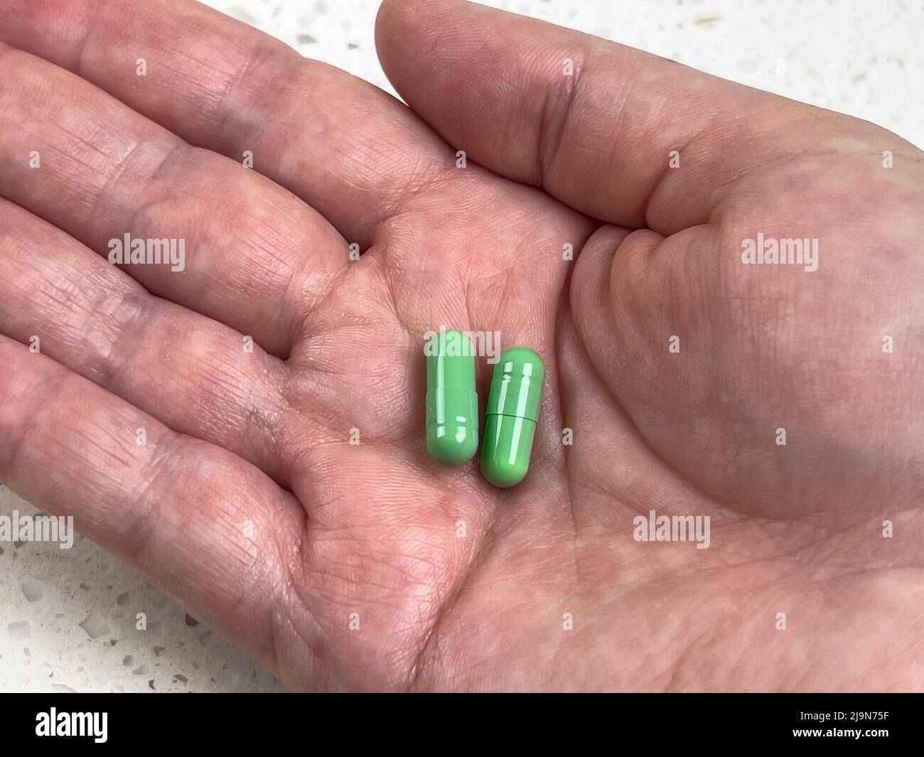 Nahaufnahme von zwei grünen Pillen in der Handfläche einer erwachsenen Hand, vor einem hellen Hintergrund geschossen Stockfoto