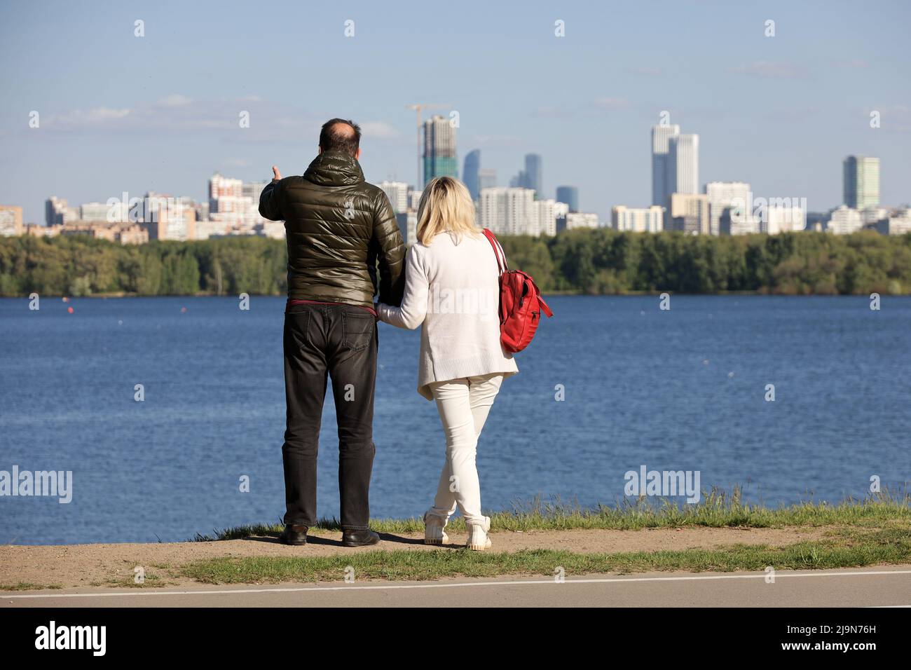Paar in Jacken, die auf dem Hintergrund von Fluss- und Stadtgebäuden stehen. Romantische Reise und Urlaub, die Wahl der Immobilie Stockfoto