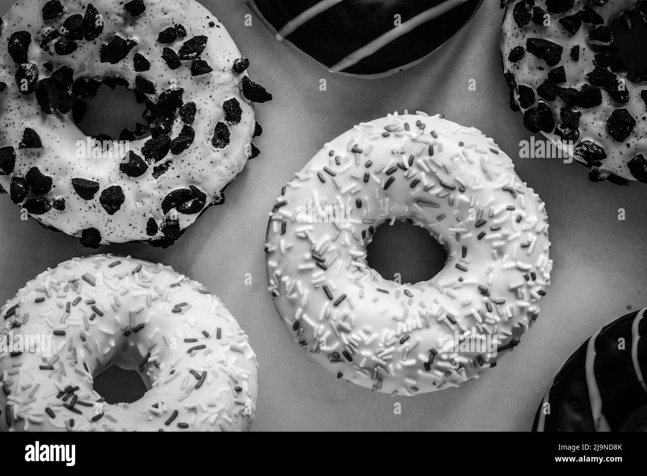 Flaches Lay-Bild von Ringdonut mit weißer Glasur und hunderttausenden anderen Donuts, schwarz-weiß-Bild Stockfoto