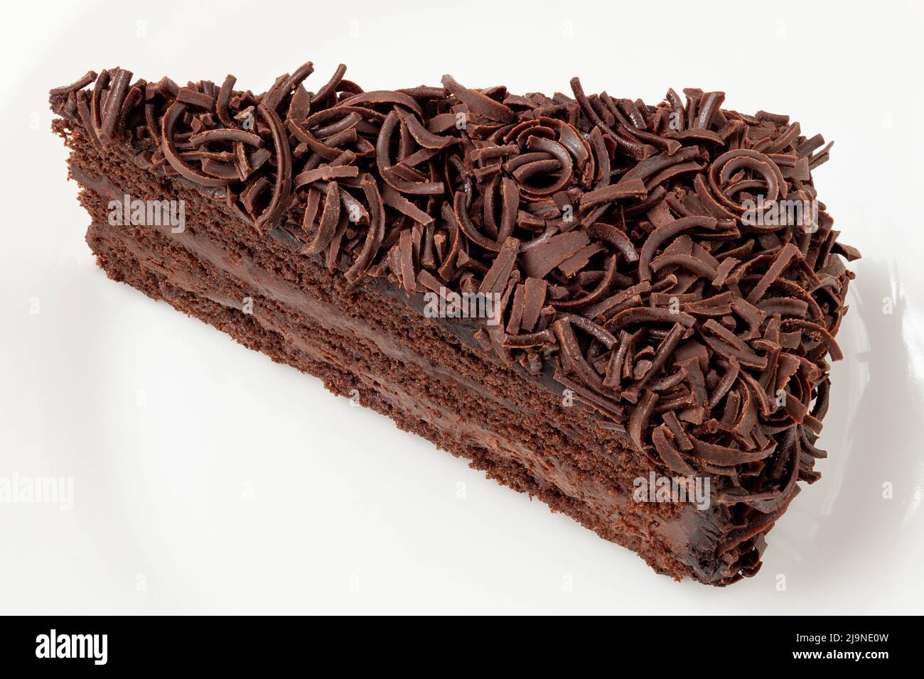 Scheibe Schokoladenkuchen mit Sahnefüllung und auf weißem Teller isoliertem Schokoladenspan. Draufsicht. Stockfoto