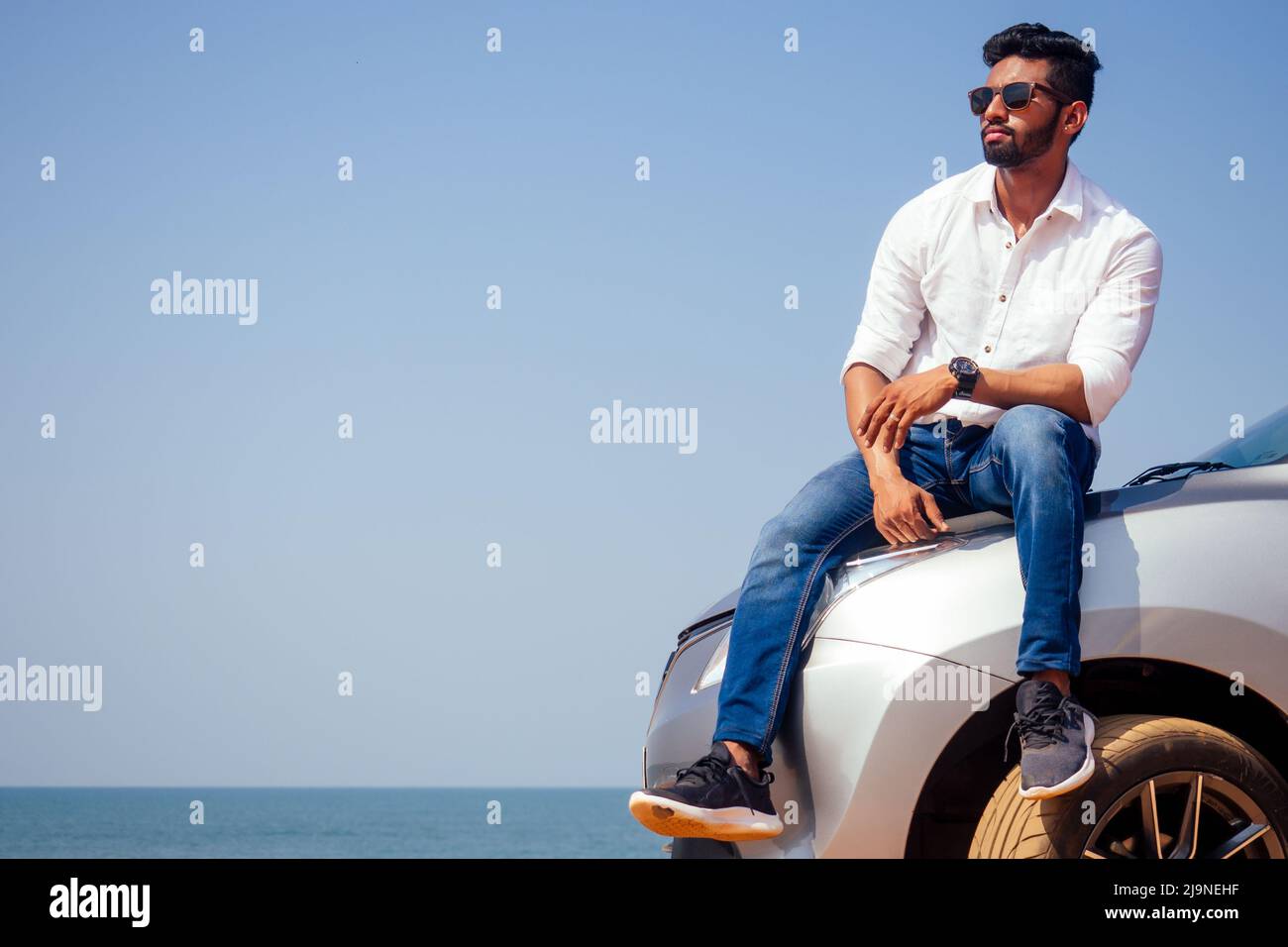 Erfolgreiche junge Geschäftsmann Sonnenbrille am Strand. Afro-Mann, der sich auf seinem Auto vor dem Meer auf der Straße geparkt hat, genießt Ruhe und Stille Stockfoto