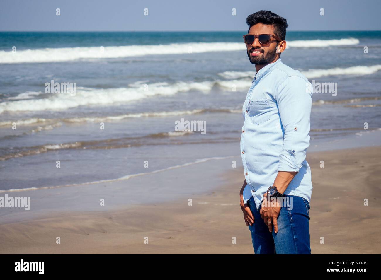 Junger afroamerikanischer Mann in blauem Hemd und Jeans am Meeresstrand. Stockfoto