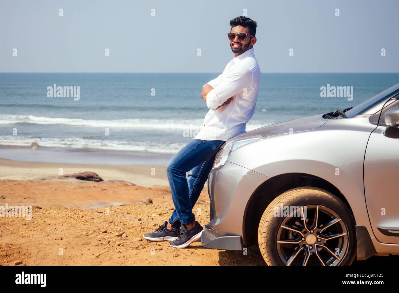 Erfolgreiche junge Geschäftsmann Sonnenbrille am Strand. Afro-Mann, der sich auf seinem Auto vor dem Meer auf der Straße geparkt hat, genießt Ruhe und Stille Stockfoto