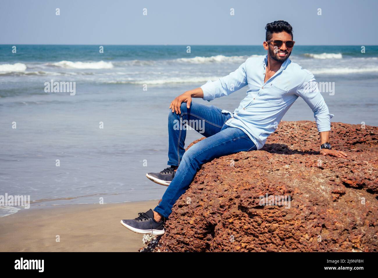 Junger afroamerikanischer Mann in blauem Hemd und Jeans am Meeresstrand. Stockfoto
