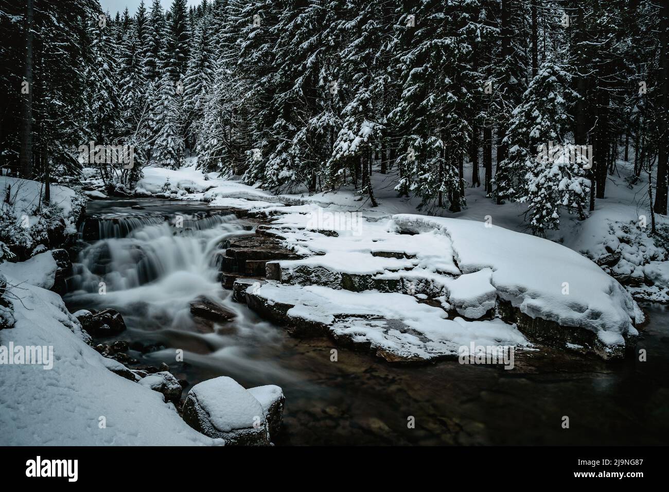 Winterwasserfall und Kaskaden im Riesengebirge in der Nähe von Spindleruv Mlyn, Tschechische Republik. Verschneite gefrorene Landschaft. Wilder Strom, Gelassenheit, Reisen im Hintergrund, Stockfoto