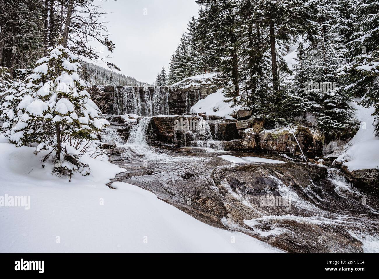 Winterwasserfall namens Certova strouha in Riesengebirge, Tschechische Republik. Verschneite gefrorene Landschaft. Gefrorener Wasserfall und Wildbach, lange Exposition wat Stockfoto