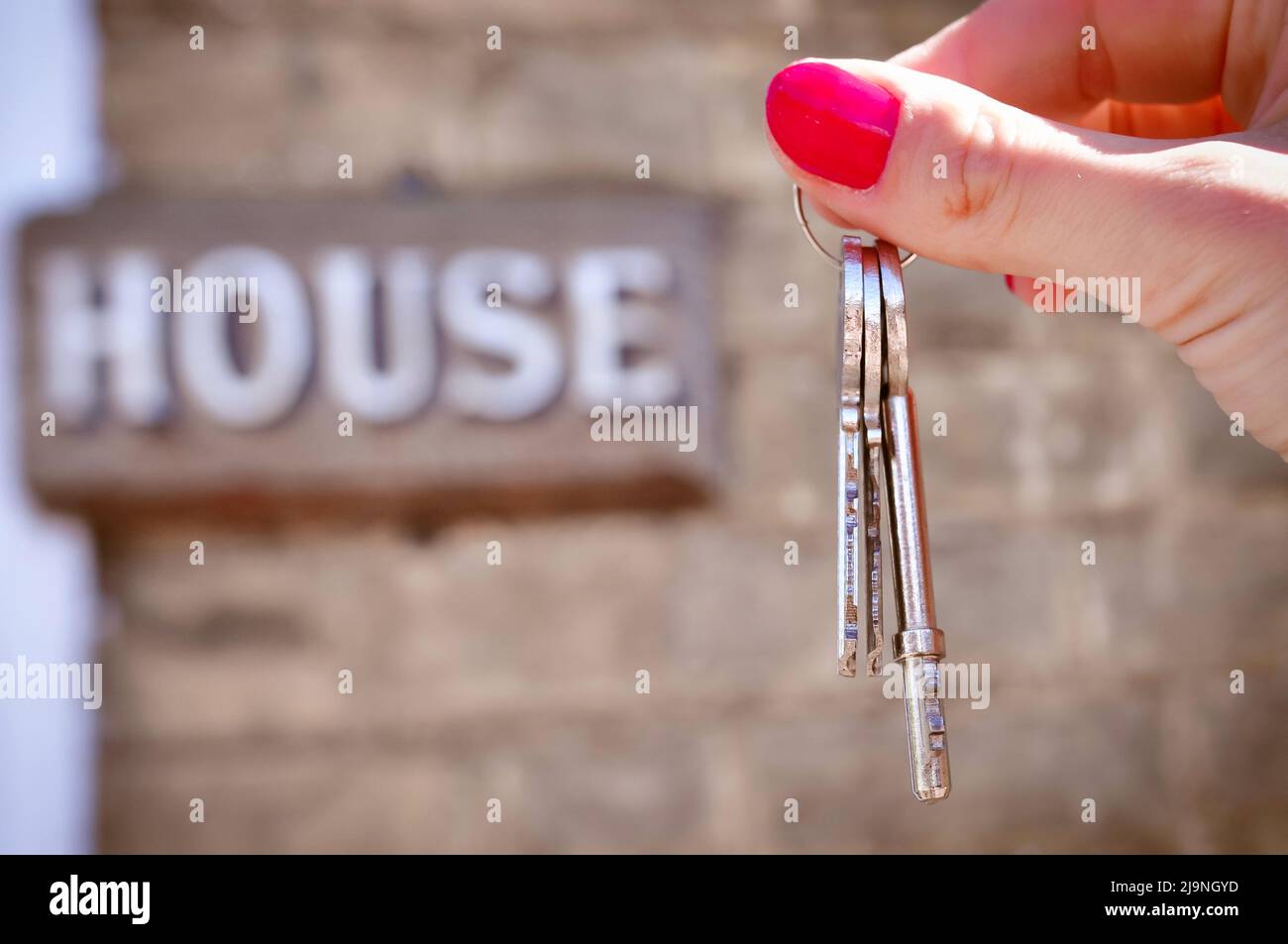 Frauenhand mit Metallschlüsseln auf verschwommenem Hintergrund mit Haus Stockfoto