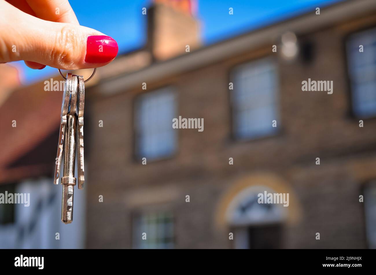 Frauenhand mit Metallschlüsseln auf verschwommenem Hintergrund mit Haus Stockfoto