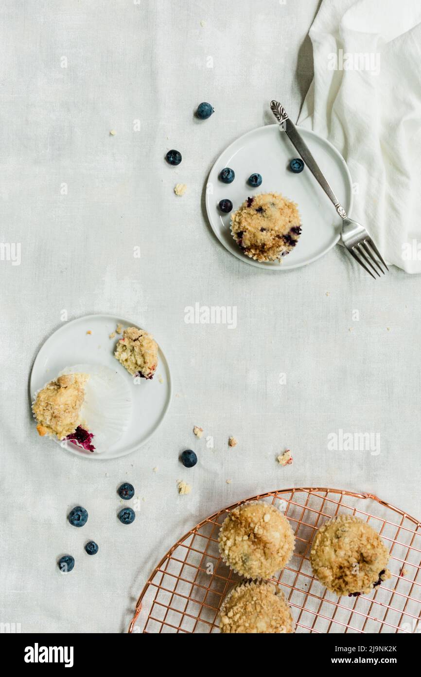 Heidelbeer-Muffins auf Marmorboden mit silbernen und kupferfarbenen Backgeräten und weißen Tellern Stockfoto