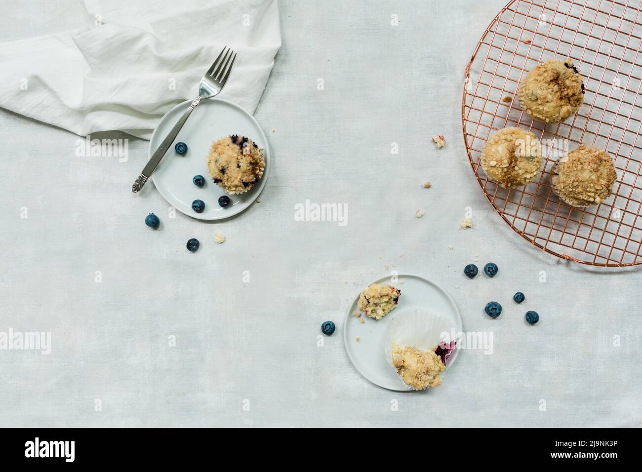 Heidelbeer-Muffins auf Marmorboden mit silbernen und kupferfarbenen Backgeräten und weißen Tellern Stockfoto