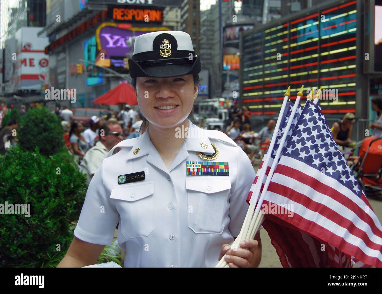 CTIC Park, eine Navy-Frau mit mehreren Medaillen, posiert mit einer Handvoll auf amerikanischen Fahnen bei einer Rekrutierungsveranstaltung. Am Times Square, New York City. Stockfoto