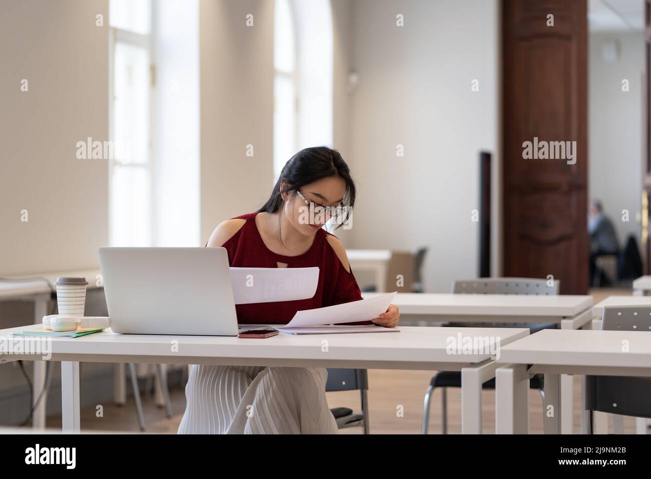 Asiatische Mädchen College-Student in Brille lesen Materialien während der Vorbereitung für Test oder Prüfung in der Bibliothek Stockfoto