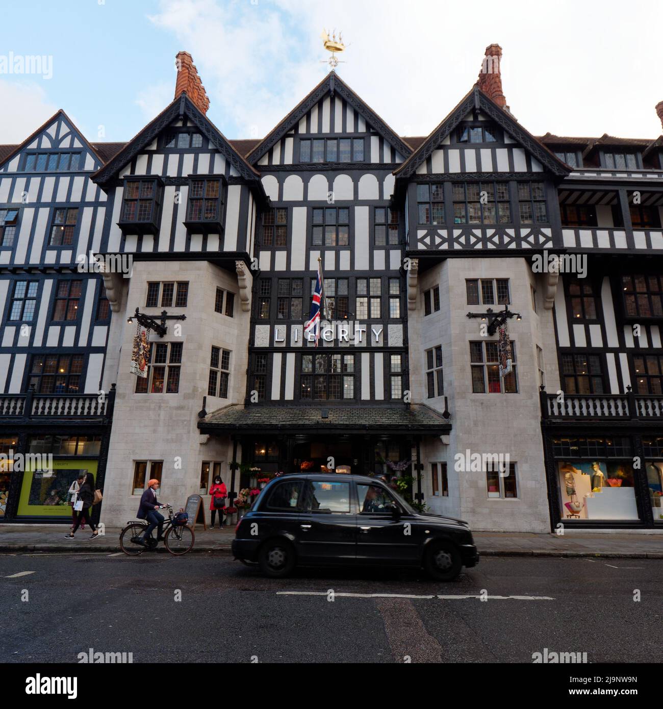 London, Greater London, England, Mai 11 2022: Taxi und ein Radfahrer mit orangefarbenem Helm vor dem Liberty-Designer-Apartment-Store Stockfoto